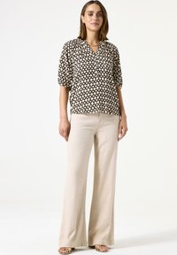 Blouse à motifs noir et blanc avec des manches courtes, décolleté en V, coupe décontractée, associée à un pantalon large beige et des sandales à lanières.