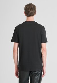 Camiseta negra de manga corta con cuello redondo, fabricada en tejido suave. Presenta un pequeño logo en el cuello y un corte regular.