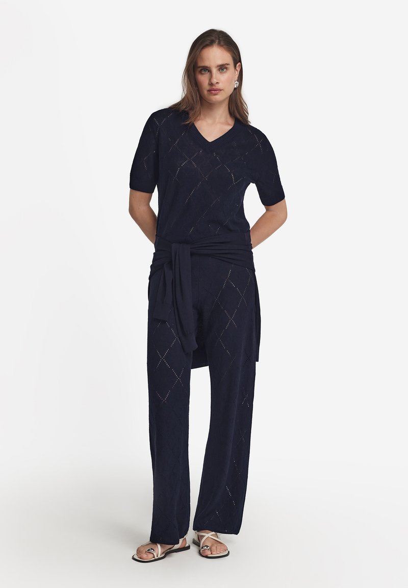Ensemble tricoté bleu marine en deux pièces avec un haut à manches courtes et un pantalon à jambes larges, présentant des motifs en losanges et un détail de taille nouée.