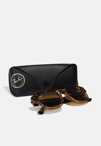 Ochelari de soare Ray-Ban în carapace maro broască, cu lentile închise la culoare, însoțiți de o etui din piele neagră cu un logo auriu.