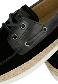 Černá lodní obuv z broušené kůže a kůže s černými tkaničkami, kovovými průchodkami, světle hnědým pleteným středovým páskem a bílou pryžovou podrážkou.