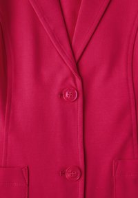 Fuksia bleiseri, jossa on muotoiltu malli, sahatut läpät, kaksi etutaskua ja yhden napin kiinnitys, samoin kuin vastaavat napit.