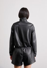 Zwarte faux leren rompert met lange mouwen, hoge kraag en een elastische tailleband. Gladde textuur en strakke lijnen, geschikt voor casual wear.