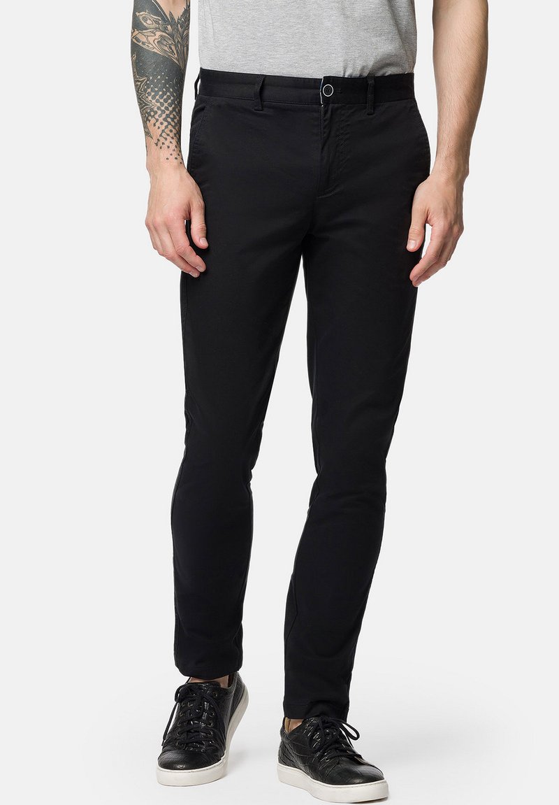 Czarne slim-fit spodnie wykonane z bawełnianego twillu, z płaskim przodem, bocznymi kieszeniami i subtelnym połyskiem, połączone z czarnymi sneakerami.