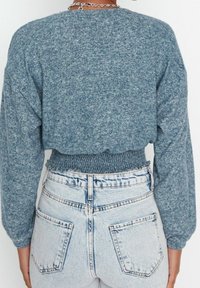 Niebieski, dziergany krótki sweter z długimi rękawami, z marszczoną talią, zestawiony z wysokim stanem jasnych dżinsów.