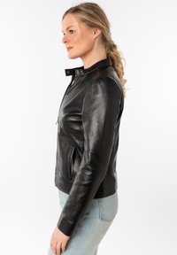 Zwarte leren jack met een getailleerd ontwerp, ritsluiting, hoge kraag en zijzakken. Gladde textuur met een licht glanzende afwerking.
