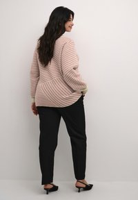 Pruhovaný svetr v jemně růžové a krémové barvě, oversized střih s kulatým zadním lemem. V kombinaci s černými tapered kalhotami a černými slingback podpatky.