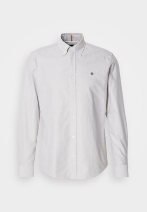 Šviesiai pilka ilgomis rankovėmis marškiniai su apykakle, baltais sagos ir maža išsiuvinėta logotipu krūtinėje. Lygus audinio tekstūra.