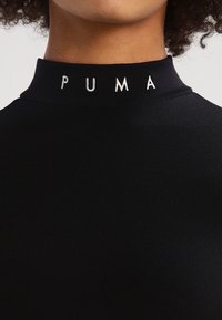 Czarny top z wysokim kołnierzem wykonany z elastycznego materiału, z białym haftowanym logo "PUMA" na kołnierzu. Gładka tekstura bez wzorów.