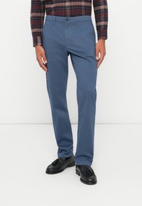 Pantaloni blu realizzati in tessuto leggero, con design a gamba dritta, chiusura con bottone e tasche laterali, abbinati a mocassini neri.
