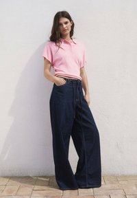 Polo shirt rosa chiaro con maniche corte, abbinato a pantaloni in denim scuro a gamba larga, con vita alta e tasche frontali.
