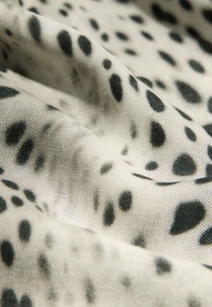 Textil con fondo beige y patrones manchados negros. La tela parece suave con una textura lisa, mostrando pliegues suaves.