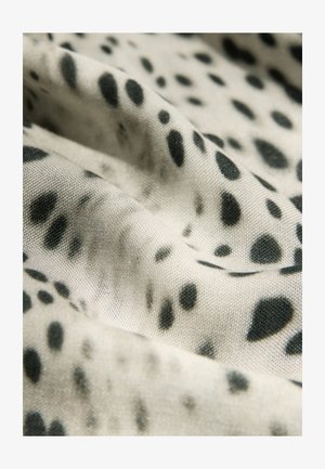 Textil con fondo beige y patrones manchados negros. La tela parece suave con una textura lisa, mostrando pliegues suaves.