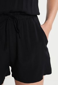 Czarne szorty wykonane z lekkiego materiału, z elastycznym pasem, detalem na sznurku oraz bocznymi kieszeniami. Gładka tekstura, casualowy design.