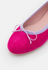 Ballerines en suède rose avec un bout arrondi, des détails en lavande et un petit nœud à l'avant. Doublure intérieure lisse.