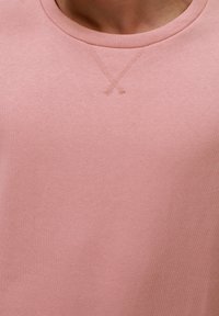 Svetle růžový svetr s kulatým výstřihem, strukturovanou tkaninou a jemným vyšívaným detailem 'X' na hrudi. Hladký, ležérní design.