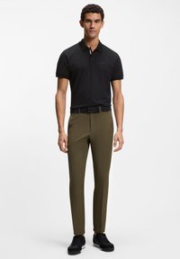 Schwarzes Poloshirt mit Muster, olivgrüne Slim-Fit-Hose und schwarze Sneaker. Glatter Stoff, kurze Ärmel und eine taillierte Passform.