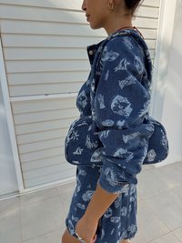 Denimantrekk med intrikate hvite grafiske trykk, som inkluderer en hettegenserjakke og matchende skjørt. Stoffet har en tekstur med synlige sømmer.