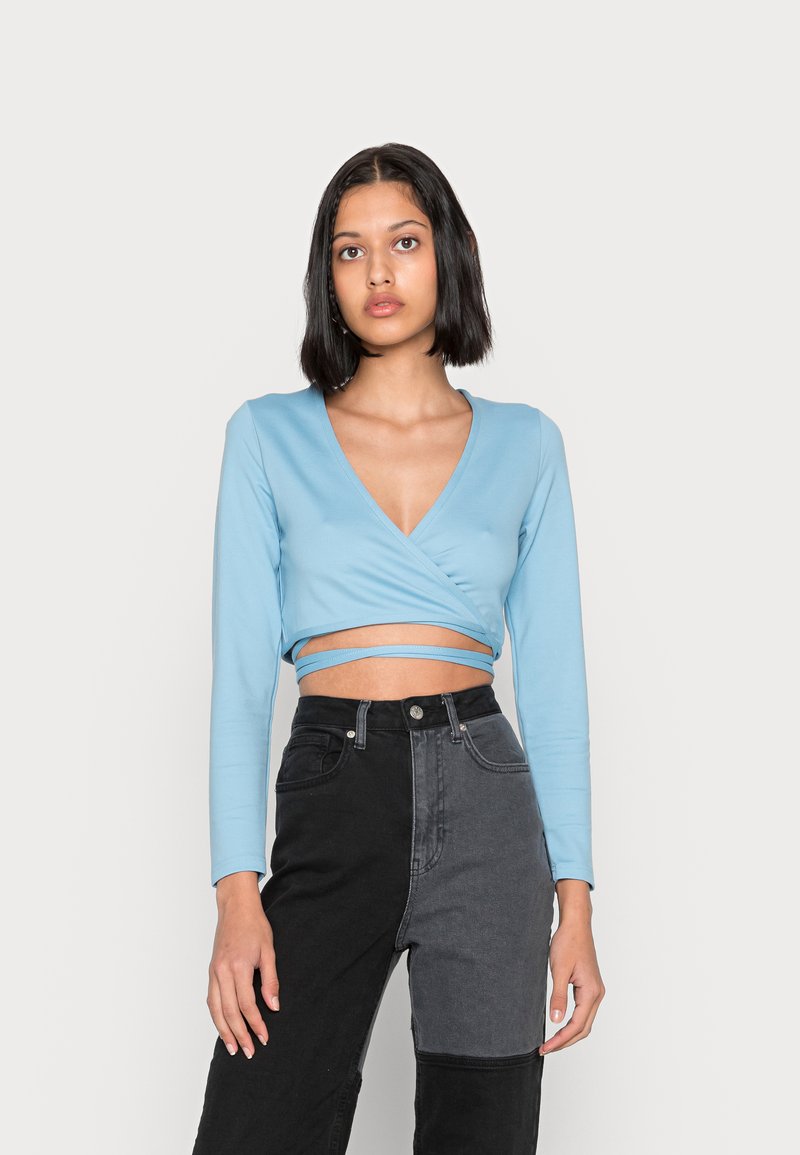 Top envolvente de manga longa azul claro com um decote em V profundo, combinado com jeans de denim de cintura alta com um design em blocos de cor preto e cinza.