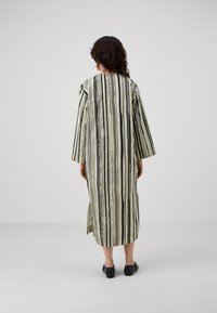 Rochie lungă, lejeră, cu dungi verticale alb-negru. Are mâneci lungi și slituri laterale pentru un confort sporit în mișcare.
