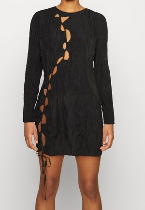 Vestido negro de manga larga con un diseño texturizado, que presenta una serie de óvalos recortados a lo largo de un lado y un detalle de cordones en el dobladillo.