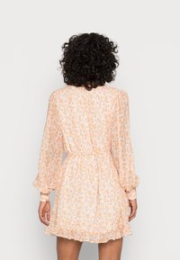 Blumenmusterkleid in sanftem Pfirsich mit langen, puffigen Ärmeln. Besitzt eine taillierte Taille und einen gerüschten Saum und ist aus leichtem Stoff gefertigt.