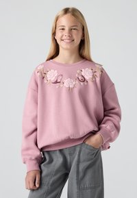 Felpa rosa chiaro con ricami floreali in tonalità di rosa e beige attorno al colletto. Presenta spalle scese e polsini a coste.