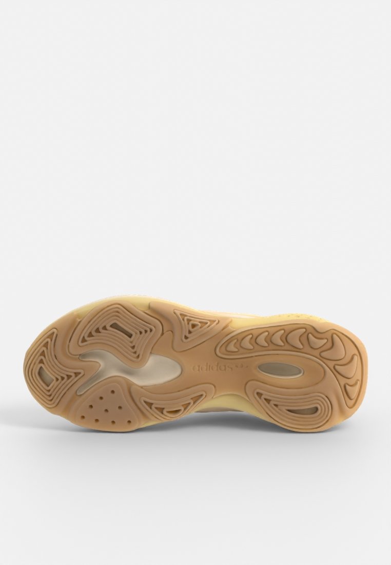 Suela de zapato de goma con surcos ondulados, de color beige y secciones texturizadas para mayor tracción. Presenta detalles en relieve del logo y orificios de ventilación.