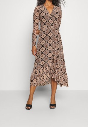 Femme portant une robe midi à manches longues avec un col en V, motif géométrique marron et noir, et ourlet volanté, associée à des talons ouverts noirs.