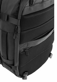 Czarny plecak z teksturowaną siateczką po bokach, wieloma zamkami i regulowanymi paskami. Wykonany z trwałego materiału i praktycznym designem.