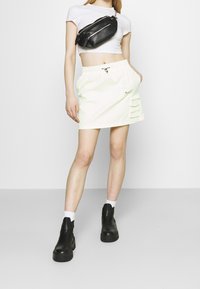 Jasnozielona mini spódnica z bocznymi kieszeniami, elastyczną talią i sznurkiem. Zestawiona z dopasowaną białą bluzką i czarnymi botkami za kostkę.