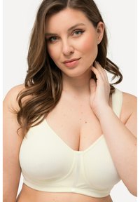 Sostén inalámbrico de color amarillo claro con una textura suave, tirantes anchos y un detalle de costura en el centro. Presenta un escote en forma de V y tela suave.
