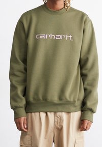Oliivinvihreä collegepaita, jossa on resorit hihansuissa ja helmassa, päällä vaaleanpunainen kirjailtu "carhartt"-logo. Valmistettu pehmeästä, teksturoidusta materiaalista.
