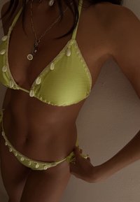 Costum de baie verde lime, cu un material texturat și accente de scoici pe margini, cu șnururi reglabile pe lateralele slipului.