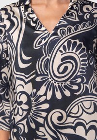 Paita tummansininen ja vaaleanbeige, jossa on V-pääntie, suuri pyörteilevä kukkakuosi ja kolmanneksen mittaiset hihat, valmistettu kevyestä kankaasta.
