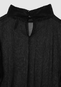 Blusa nera trasparente con pieghe verticali, apertura a chiave sulla schiena e due bottoni neri al collo. Tessuto leggero e strutturato.