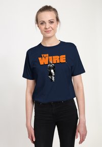 Mörkblå bomullströja med grafiskt tryck av en karaktär och texten "THE WIRE" i orange. Korta ärmar och rund halsringning.