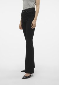 Jean noire évasée à taille haute, fabriquée à partir de denim extensible. Le design comprend une poche avant et une texture lisse et soyeuse.