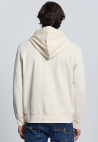 Sudadera con capucha de color crema con un corte holgado, capucha con cordón, puños y dobladillo acanalados, confeccionada con una tela suave y lisa.