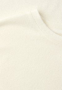 Nahaufnahme eines kremfarbenen, gestrickten Pulloverstoffs mit weicher Textur und geripptem Rundhalsausschnitt.