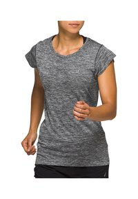 Kvinna i en grå kortärmad träningsskjorta och svarta shorts som springer mot en vit bakgrund.