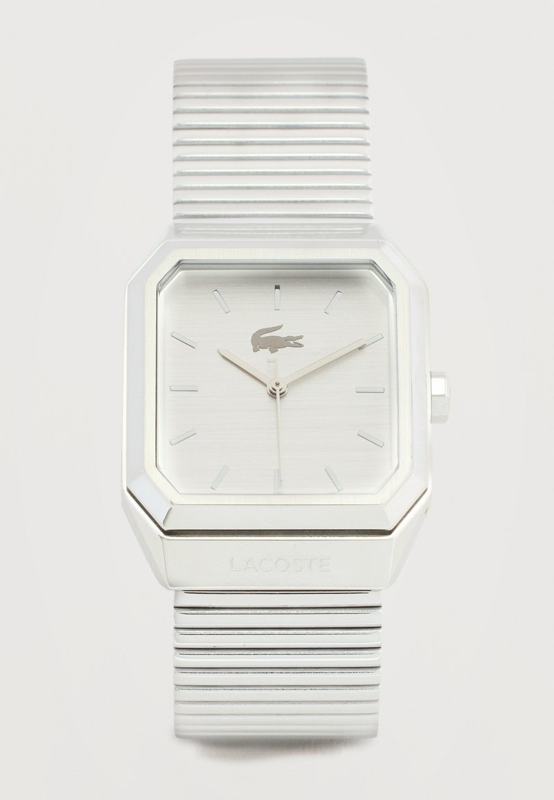 Ασημένιο τετράγωνο ρολόι χειρός Lacoste με κυματοειδές μεταλλικό λουράκι, μίνιμαλ δείκτες καντράν και λογότυπο κροκοδείλου στη θέση 12 η ώρα.