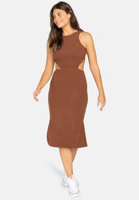 Braun geripptes Midi-Kleid mit ausgeschnittenen Seiten, ärmellosem Design und taillierter Silhouette, kombiniert mit weißen Sneakers. Glatte Textur.