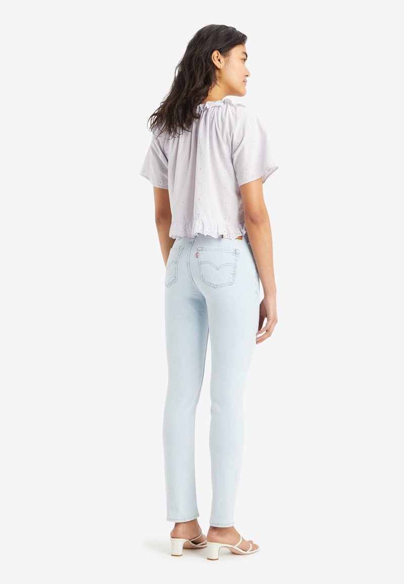 Lila Cropped-Top mit Rüschensaum und kurzen Ärmeln, kombiniert mit hellblauen Skinny-Jeans und weißen Riemchenschuhen.