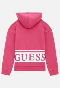 Sudadera con capucha de color rosa que presenta una banda blanca con "GUESS" impreso en letras rojas negritas en la parte posterior. Tejido suave con puños acanalados.