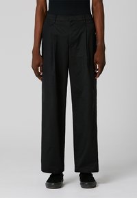 Pantalons larges noirs en tissu lisse. Comprend des plis à l'avant, une fermeture éclair et des poches latérales. Taille texturée avec passants de ceinture.