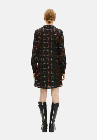 Czarna sukienka w wzory z długimi rękawami, z okrągłymi, wielokolorowymi wzorami, zestawiona z czarnymi kozakami na zamek do kolan.