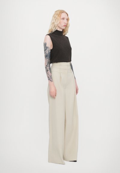Brown sleeveless turtleneck top paired with high-waisted, wide-leg beige trousers, featuring vertical seams and a smooth texture.