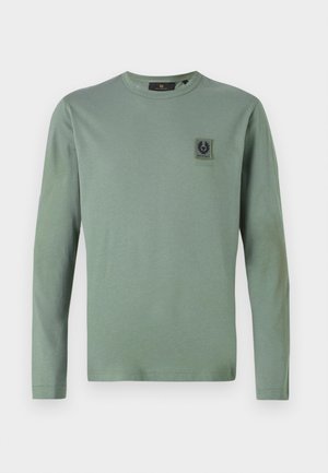 Langarm-T-Shirt in gedämpftem Grün, aus weichem Stoff. Verfügt über ein kleines schwarzes Logo-Patch auf der Brust. Rundhalsausschnitt und eng anliegende Ärmel.