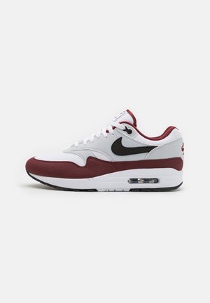 Weißer und dunkelroter Nike Air Max Sneaker mit schwarzem Swoosh-Logo, sichtbarer Luftpolstersohle und weißen Schnürsenkeln, von der linken Seite gezeigt.